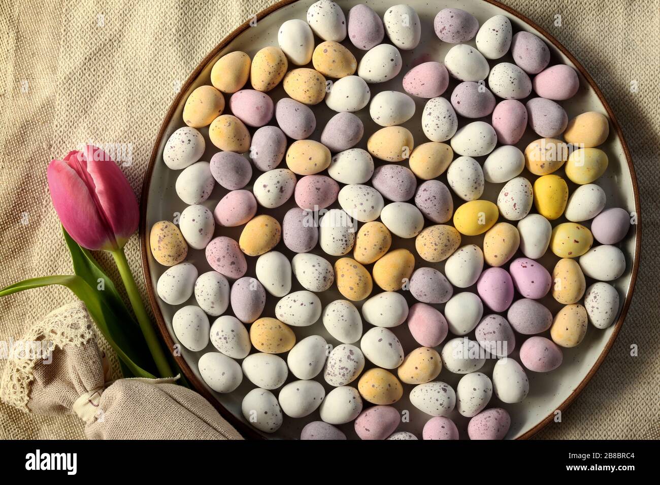 Plusieurs oeufs de Pâques colorés au chocolat sur la plaque ronde, sac cadeau en toile, bouquet de fleurs bleu printemps. Mise à plat, vue de dessus. Pâques, symbole du printemps Banque D'Images