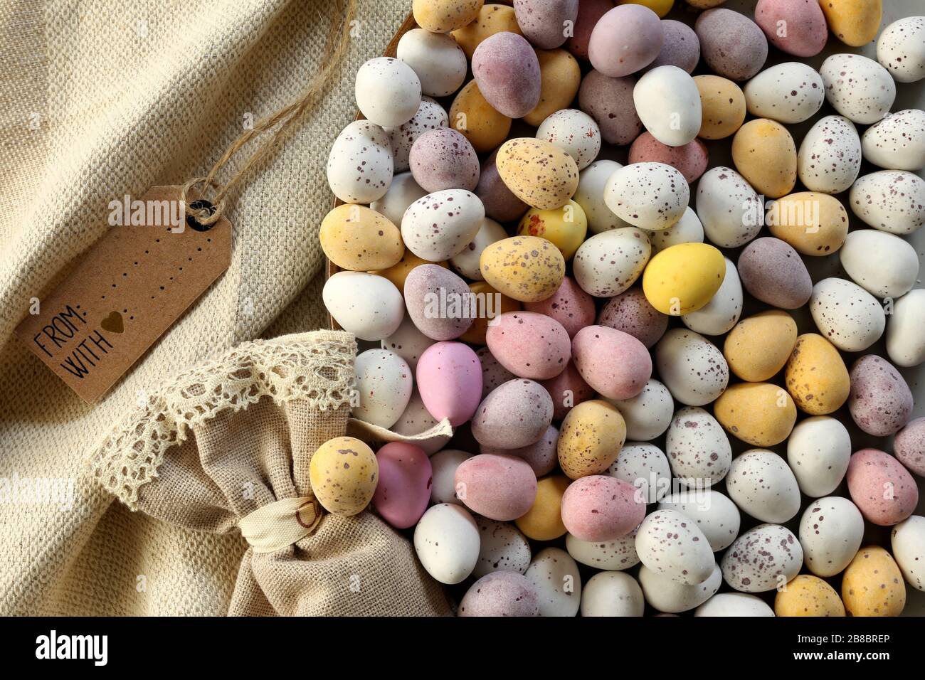 Plusieurs oeufs de Pâques colorés au chocolat sur la plaque ronde, sac cadeau en toile, bouquet de fleurs bleu printemps. Mise à plat, vue de dessus. Pâques, symbole du printemps Banque D'Images