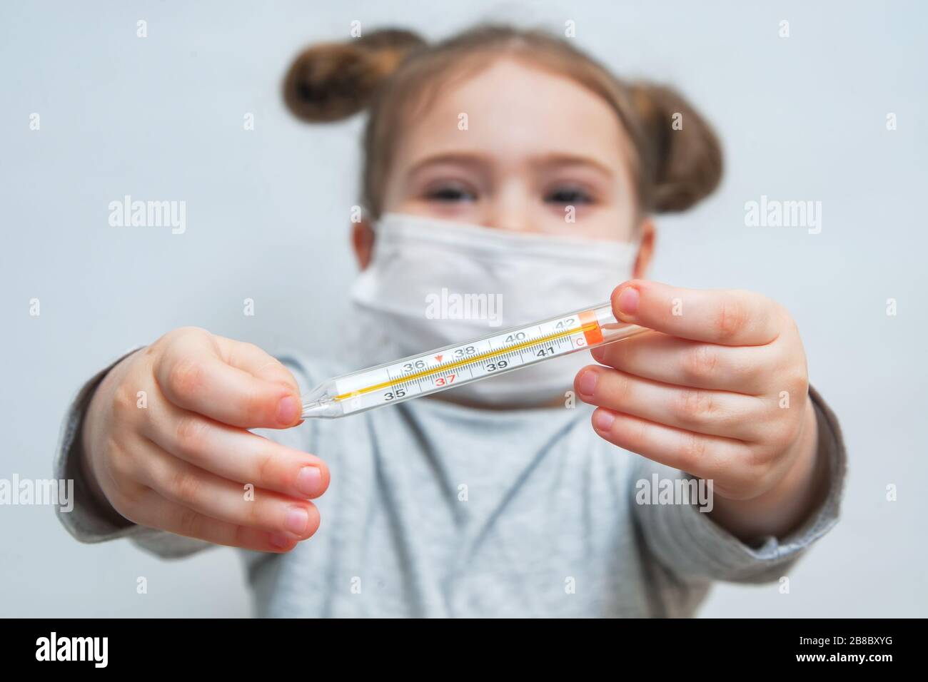 Une petite fille dans un masque médical montre le thermomètre. Concept médical de la période épidémiologique, des maladies respiratoires et des températures élevées Banque D'Images