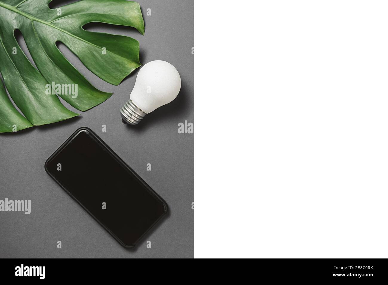 Créativité inspiration, idées concepts avec ampoule, feuille verte monstera et smartphone moderne avec espace de copie sur fond gris et blanc minimum Banque D'Images