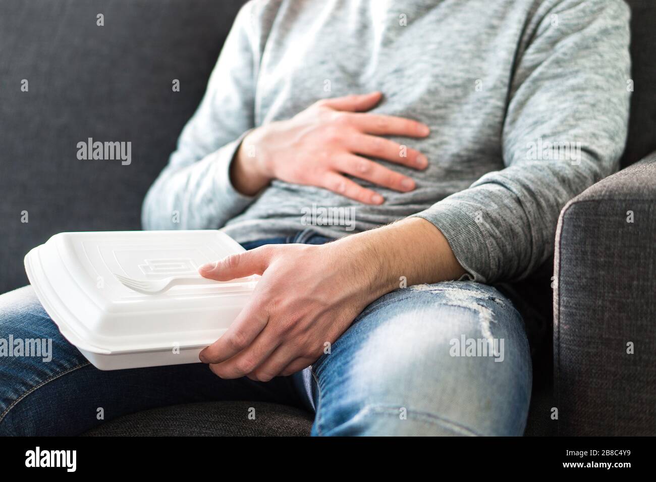 Après avoir mangé de la nourriture rapide. L'homme se sent plein ou prend la sieste après avoir mangé des indésirables. Guy ayant hange ou mauvaise alimentation. Douleurs à l'estomac en étant assis sur le canapé. Banque D'Images