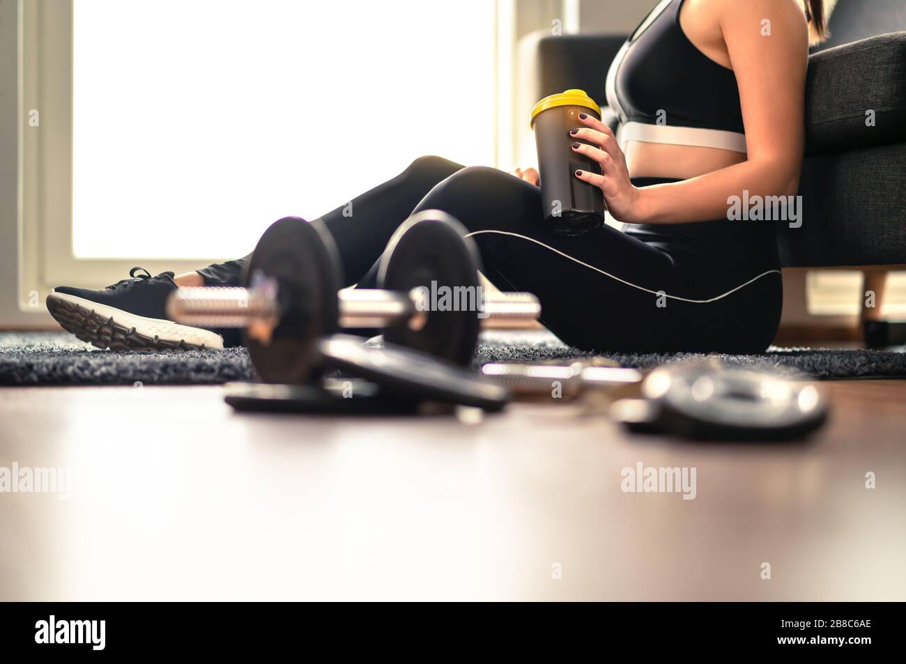 Femme de fitness buvant des protéines ou des boissons de récupération après l'entraînement et l'entraînement de poids. Faire de l'exercice à la maison. Dame dans des vêtements de sport qui se tiennent secoué. Banque D'Images