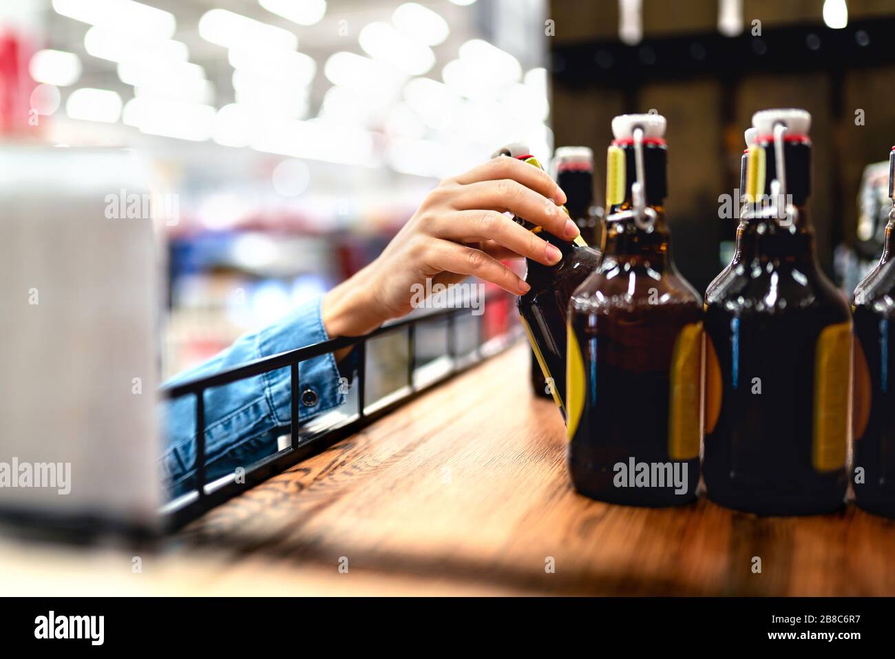 Le client prend une bouteille de bière à l'étagère du magasin de spiritueux. Femme faisant du shopping dans l'alcool ou le personnel du supermarché remplissant et stockant des étagères dans l'allée des boissons. Banque D'Images