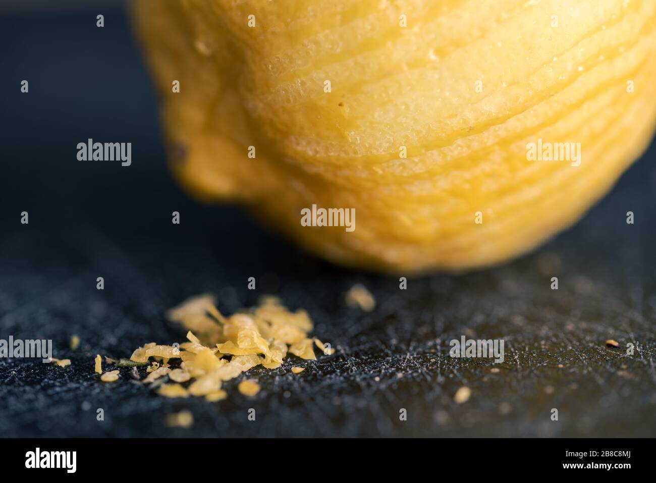 Détail de petits morceaux de zeste de citron avec le citron de laine en arrière-plan allongé sur le tableau noir de découpe Banque D'Images