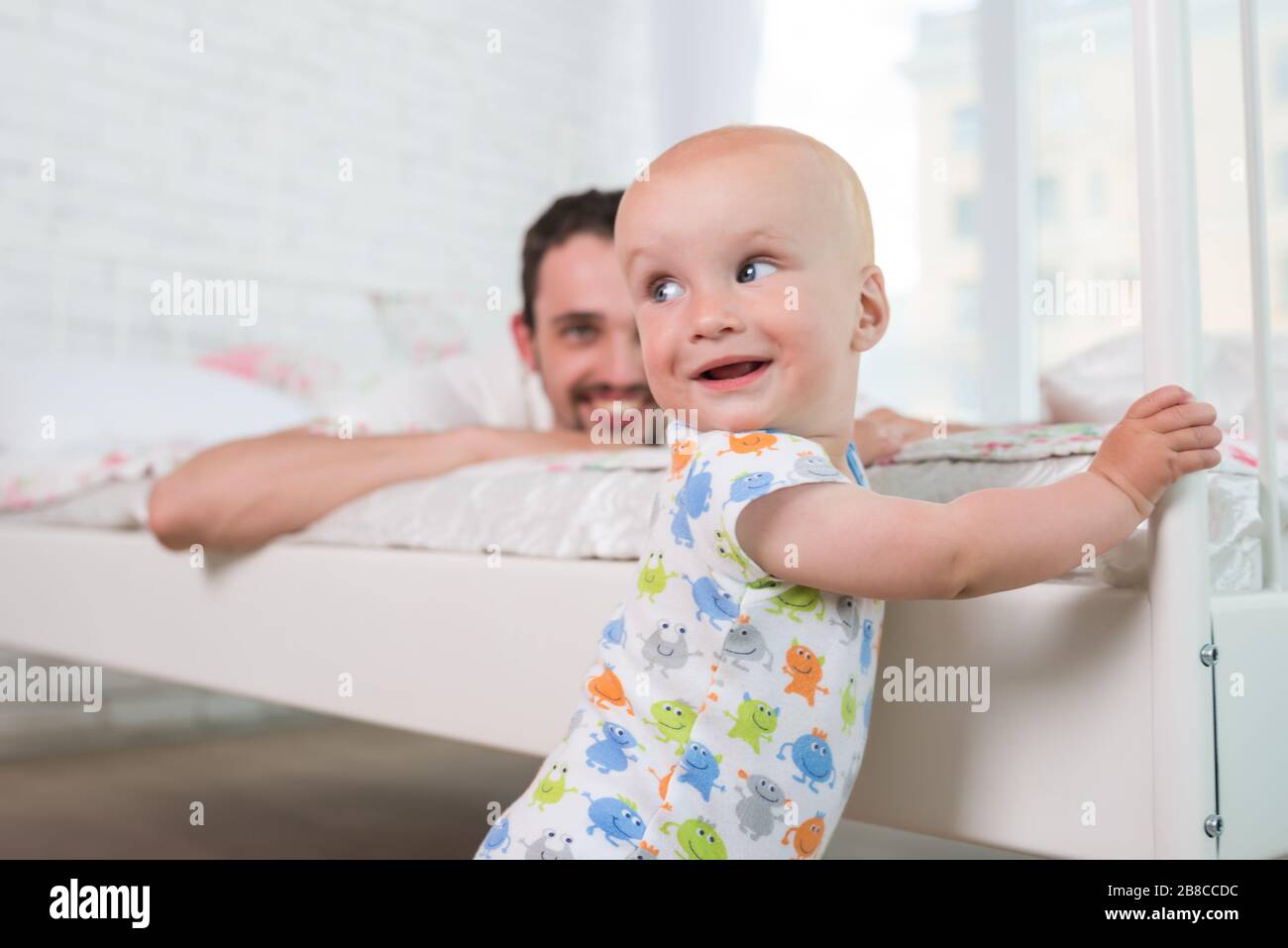 Le Joli Petit Bebe Est Debout Sur Le Bord Du Lit Qui Tient Sur La Tete De Lit Contre Le Fond De Ses Parents Concept De Heureux Nouvellement Fait Par Photo Stock