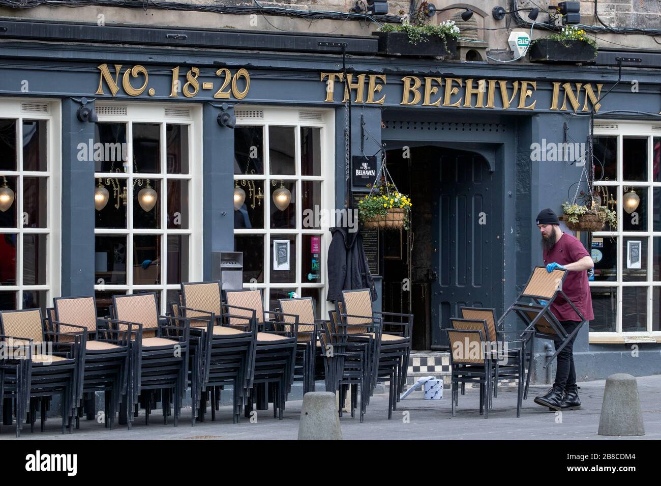 Un membre du personnel du Beehive Inn à Grassmarket, Édimbourg, nettoie et met les chaises après la fermeture du pub en raison de l'éclosion de coronavirus. Banque D'Images