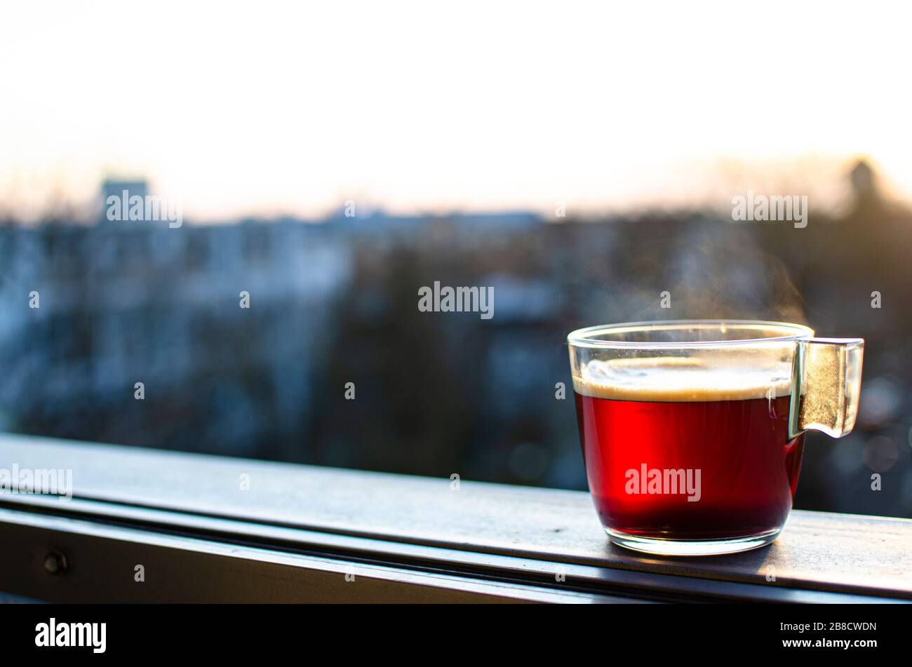 Tasse en verre de thé chaud, boisson chaude avec fond flou de la ville. Boisson rouge. Café. Banque D'Images