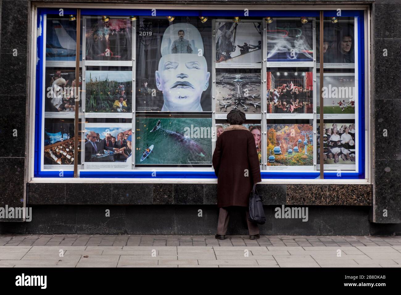 Moscou, Russie. 21 mars 2020 une vieille femme regarde des photos de l'agence de presse TASS pour 2019 ans exposées sur la façade du bâtiment de l'agence au centre de Moscou, Russie Banque D'Images