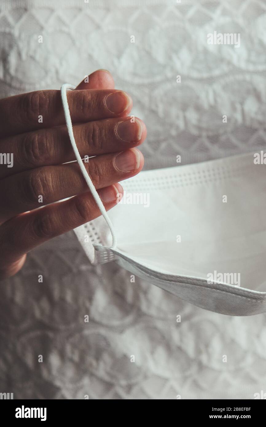 Les mains de la mariée tenant le masque médical blanc. Femme en robe de mariage pendant l'épidémie de Coronavirus. Mariages annulés ou différés causés par l'éclosion de COVID-19. Concept de coronavirus, photo conceptuelle. Banque D'Images