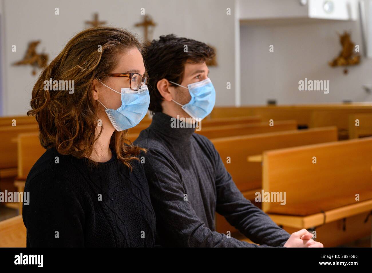 Un jeune couple en masques de visage priant dans une église pendant la pandémie COVID-19. Bratislava, Slovaquie. Banque D'Images