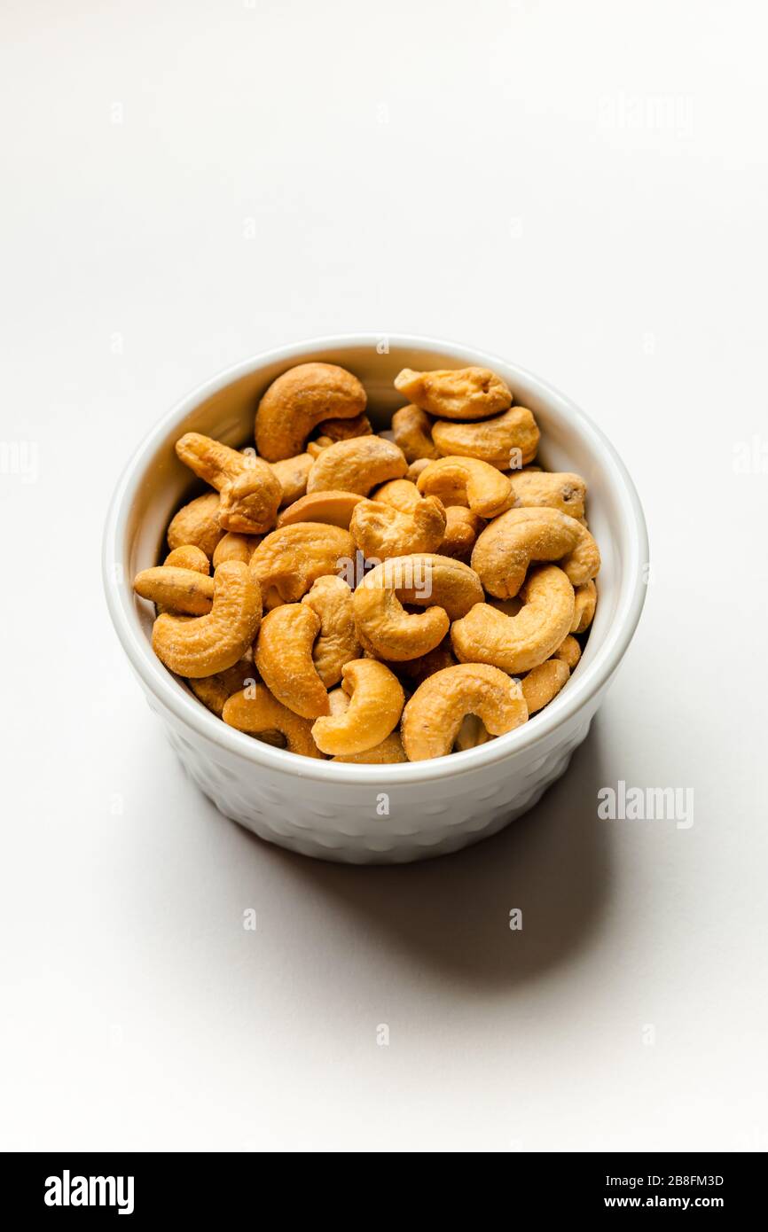 Un petit bol blanc de délicieux noix de cajou salées saines isolées sur un fond blanc haut vers le bas Banque D'Images