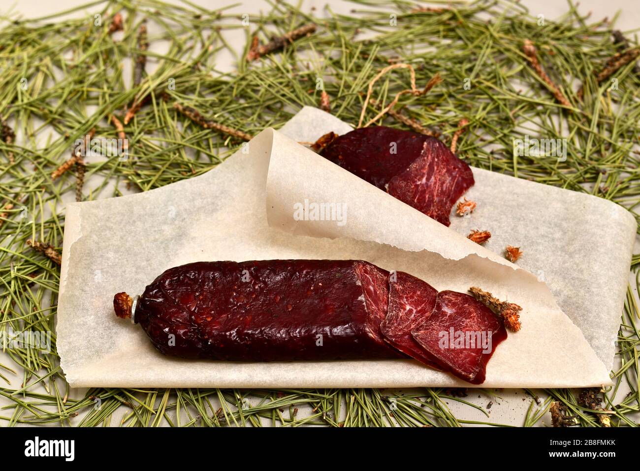 Saucisses séchées à base de viande de roe sur parchemin avec des bourgeons de pin. Parquet en aiguilles de pin. Banque D'Images