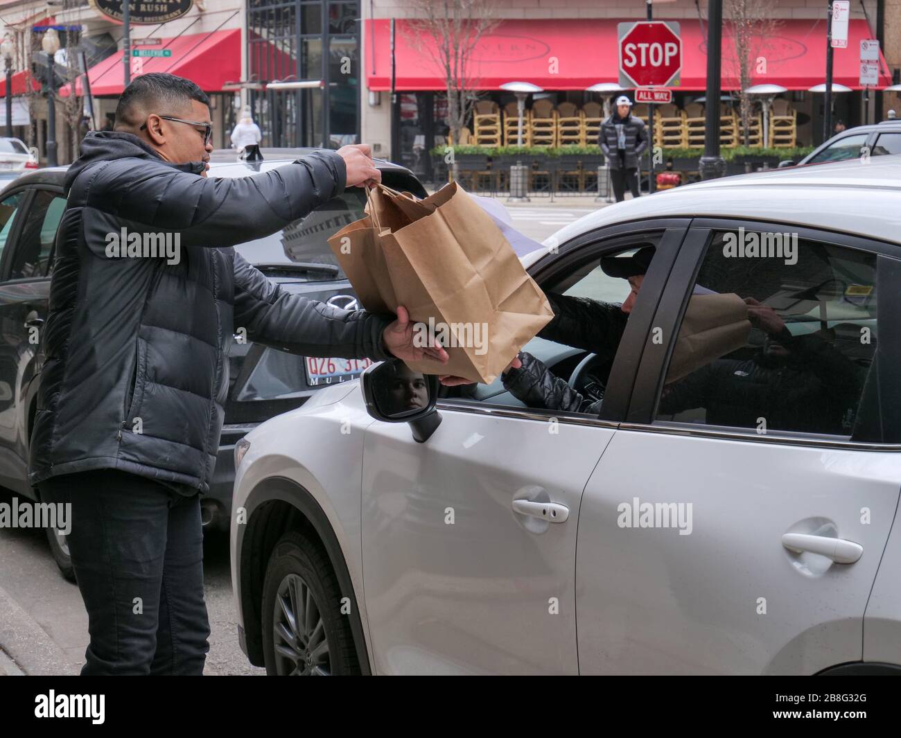 Chicago, Illinois, États-Unis. 21 mars 2020. Un employé du restaurant livre un ordre de prise pour le ramassage à bord d'un trottoir à un véhicule sur la rue Rush. Les restaurants ne sont ouverts qu'à la sortie ou à la livraison par mesure de précaution contre la propagation de COVID-19. Governor Pritzker a émis un séjour à la maison à partir de 17:00 heure locale aujourd'hui. Banque D'Images