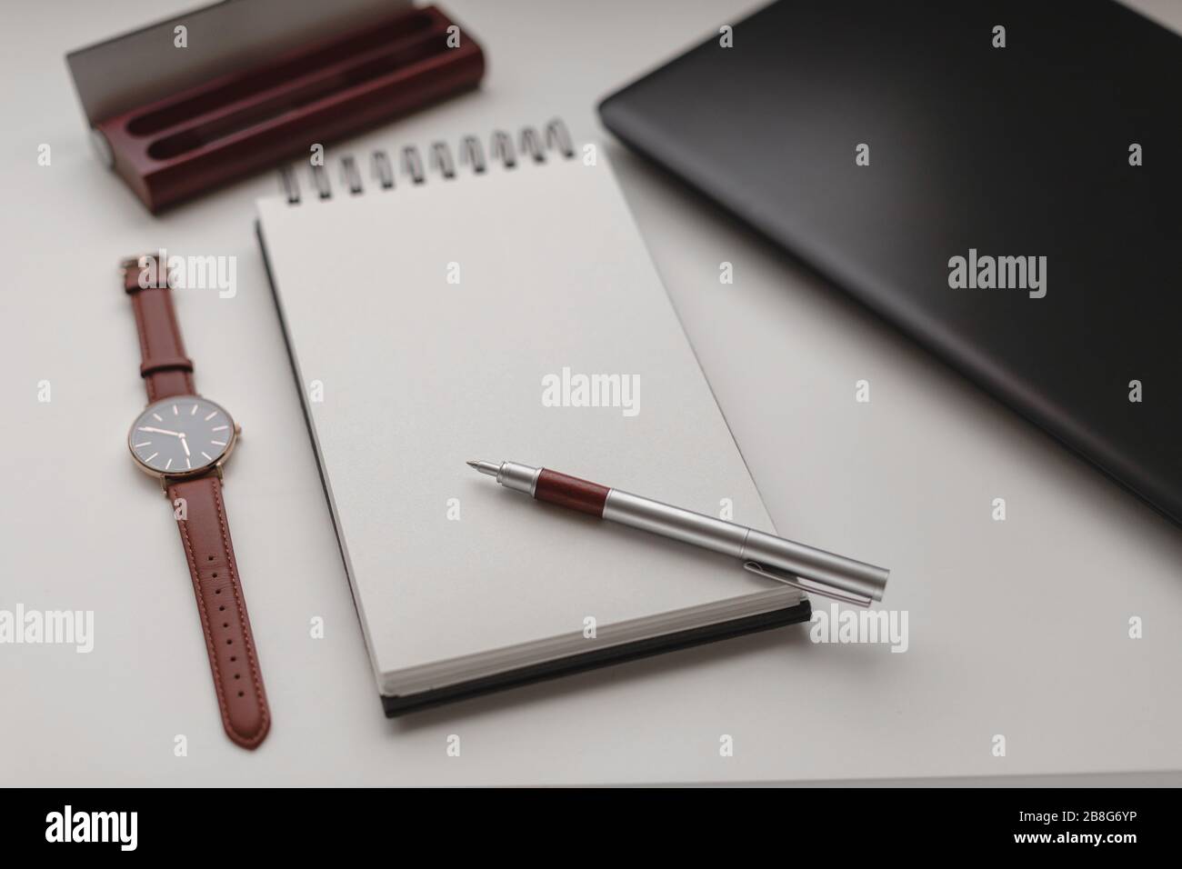 Angle de vue élevé d'un bloc-notes en spirale ouvert avec une feuille vierge et un arrière-plan de travail. Ordinateur portable, stylo, étui à stylet et montre. Travail, affaires, freelan Banque D'Images