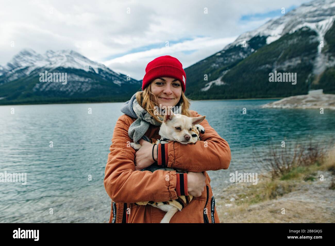 une fille dans une veste orange tient une chihuahua dans ses bras près du lac, au canada Banque D'Images