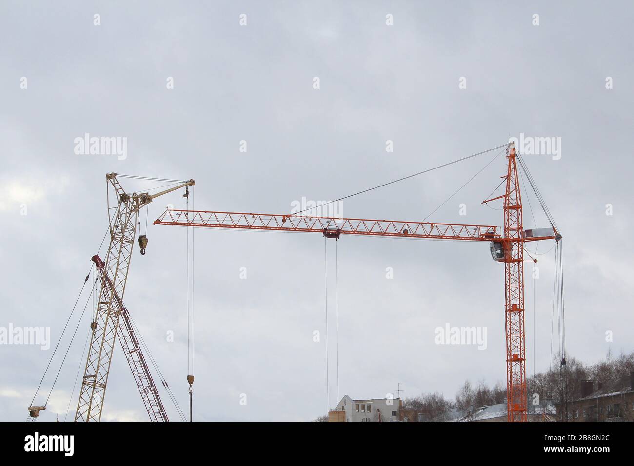 Plusieurs grues de construction travaillent sur un chantier. Silhouettes contre le ciel blanc. Banque D'Images