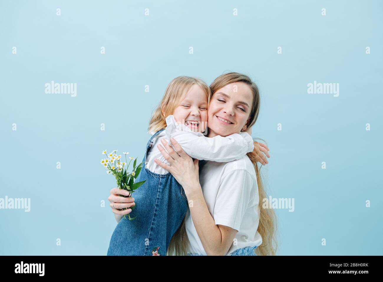 La petite fille reçoit un hug de sa mère pour donner le bouquet de chamomilles sauvages Banque D'Images