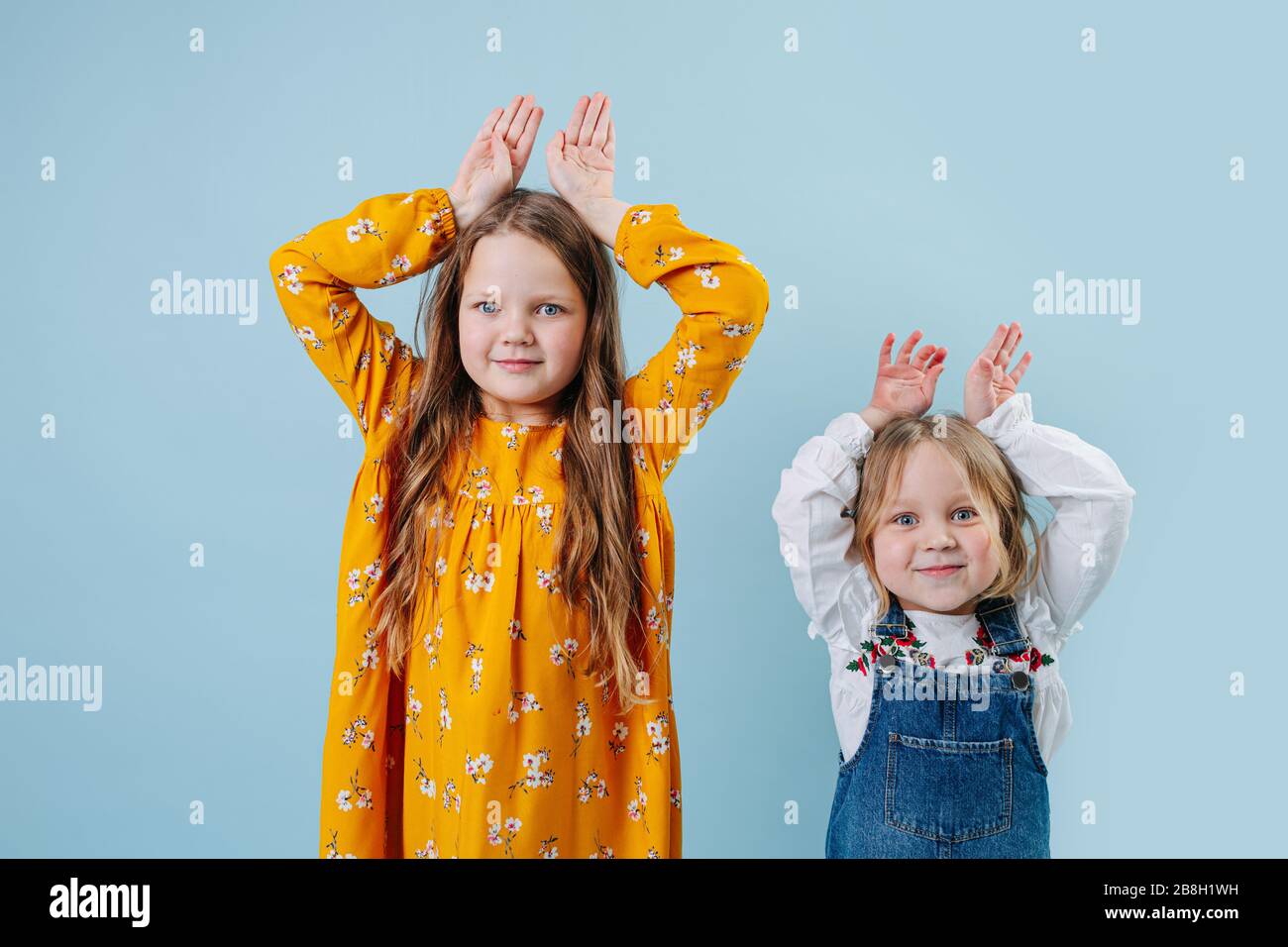 Fynny petites sœurs faisant le geste des oreilles de lapin de pâques avec les mains sur le bleu Banque D'Images