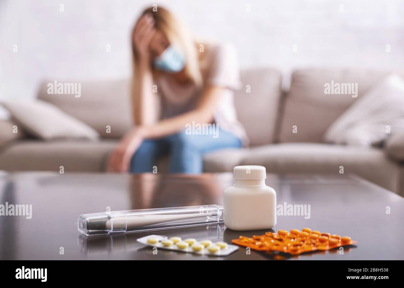 Concentrez-vous sur les pilules et le thermomètre. Fille malade dans le masque de protection assis sur le canapé Banque D'Images