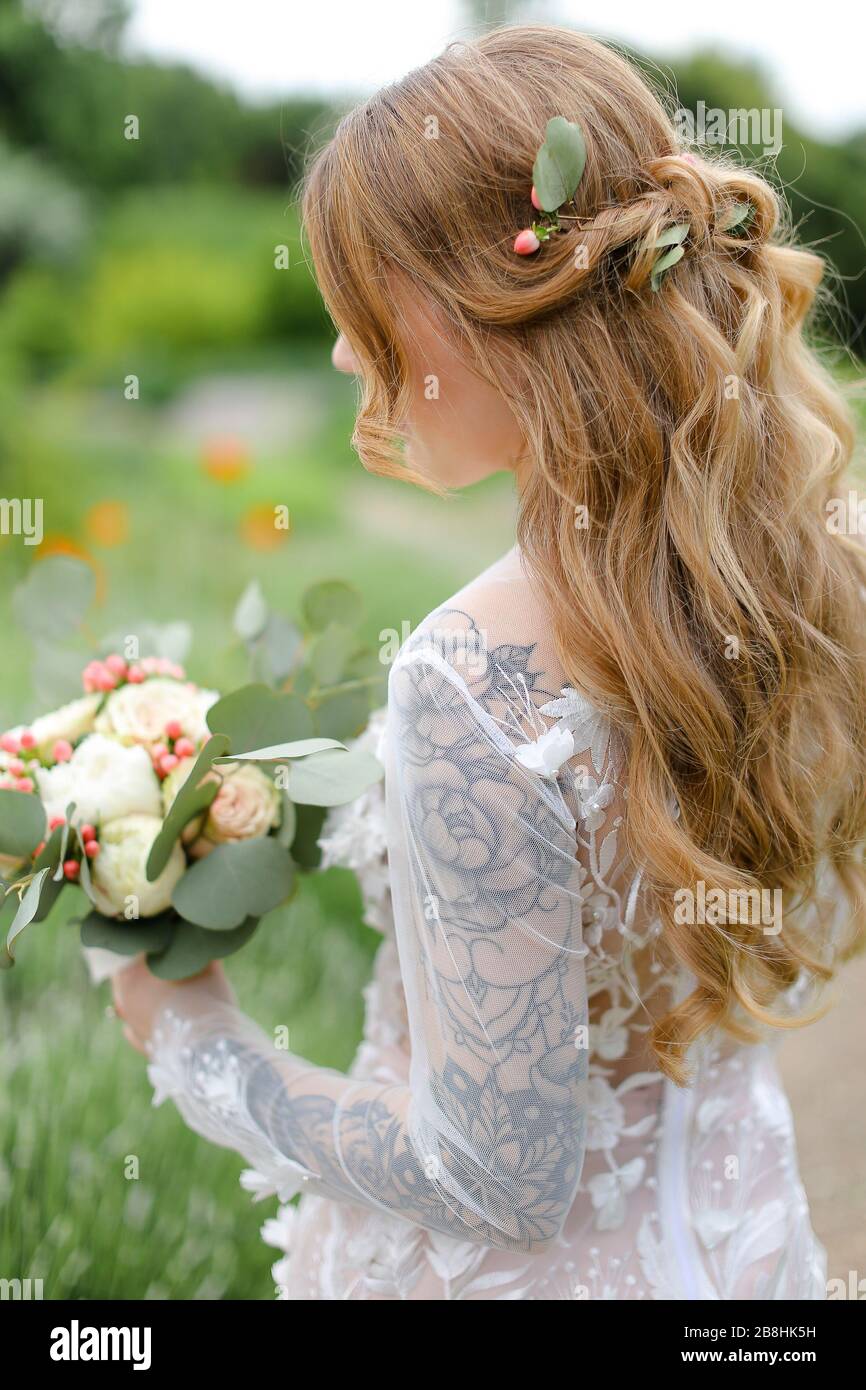 Vue arrière portrait de la mariée avec bouquet marchant dans le champ. Banque D'Images