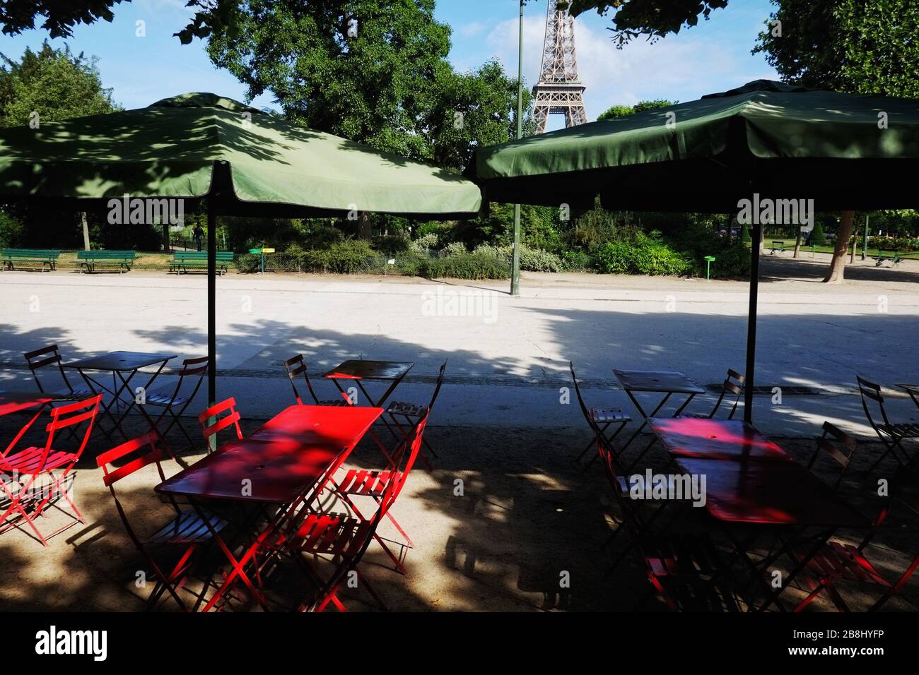 Café français en plein air, parasols verts & tables rouges sur l'avenue Charles Risler, champ de Mars été avec un aperçu de la Tour Eiffel à travers les arbres du parc Banque D'Images