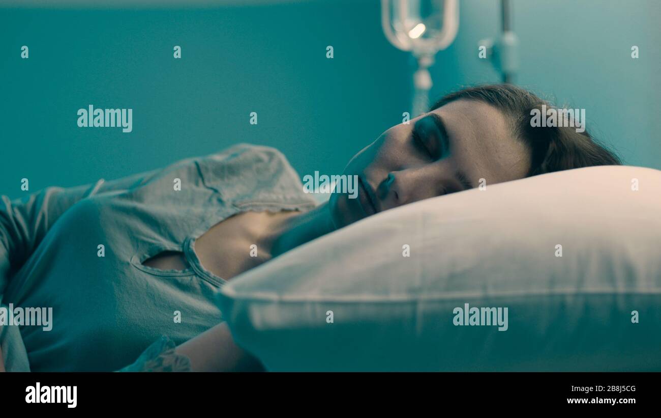 Jeune femme allongé dans un lit d'hôpital la nuit et dormant avec perfusion IV Banque D'Images