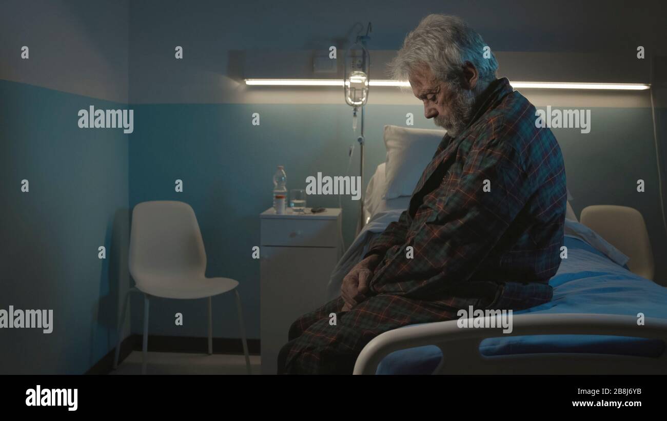 Homme senior déprimé assis seul sur le lit de l'hôpital la nuit, il se sent seul et abandonné Banque D'Images
