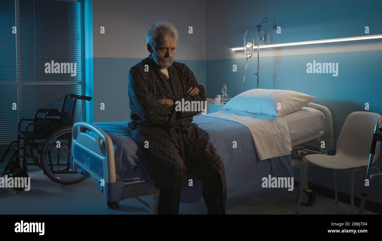Homme senior déprimé assis seul sur le lit de l'hôpital la nuit, il se sent seul et abandonné Banque D'Images
