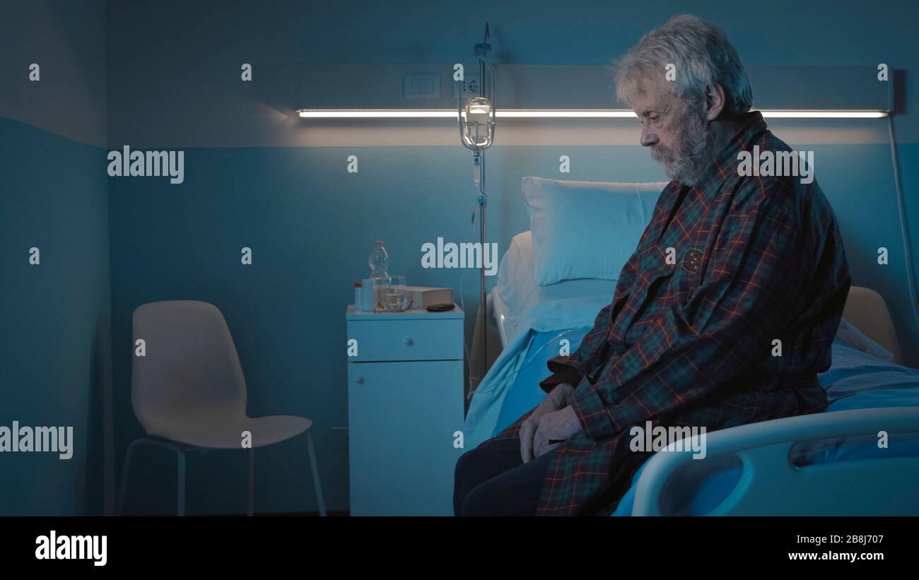 Homme senior déprimé assis seul sur le lit de l'hôpital la nuit, il se sent seul et abandonné Banque D'Images