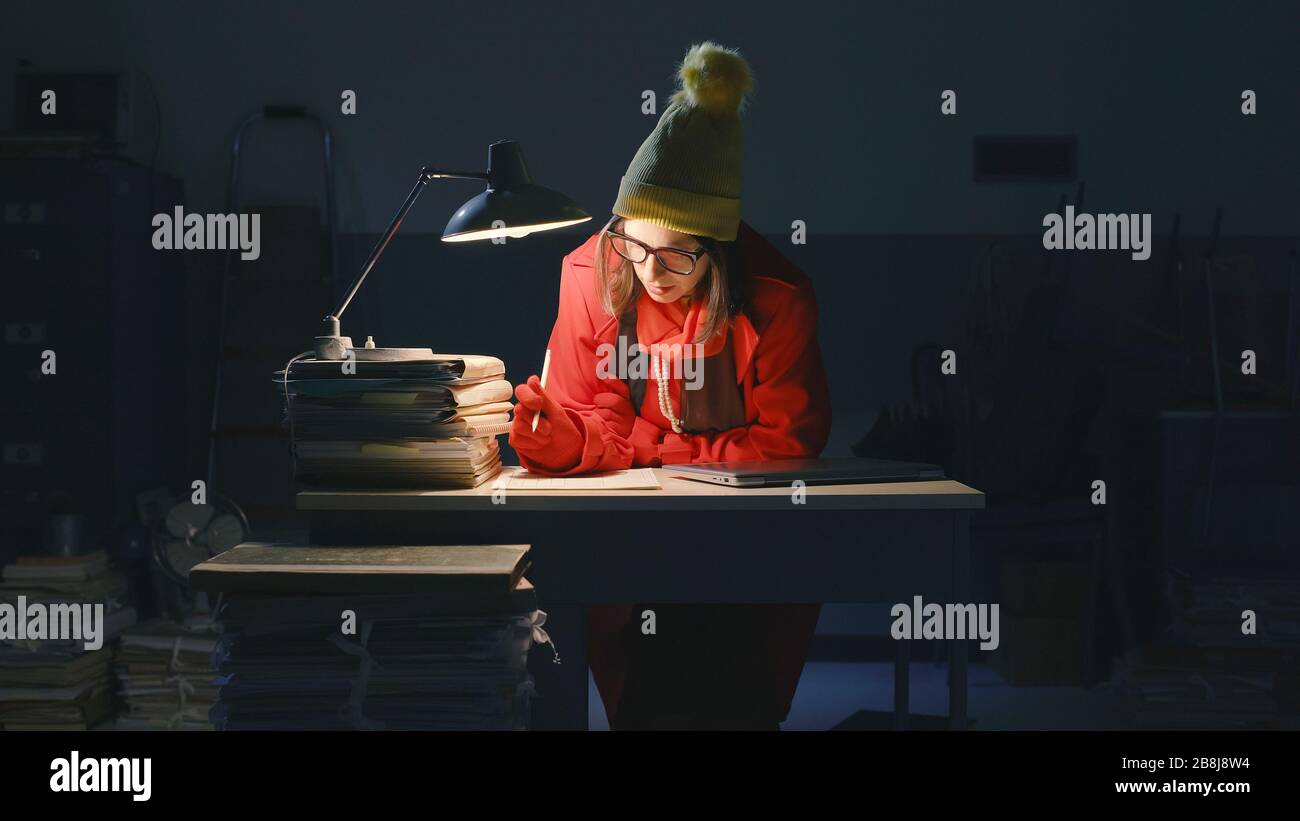 Femme d'affaires travaillant tard dans la nuit au bureau et verglaçante, elle porte un chapeau de laine et un manteau Banque D'Images