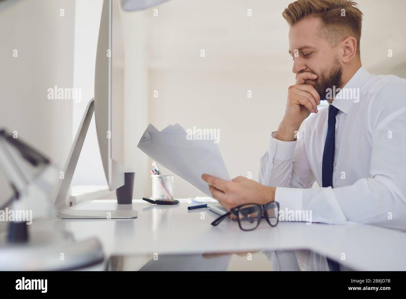 Un homme d'affaires très occupé lit les documents de travail assis à une table avec un ordinateur au bureau. Banque D'Images