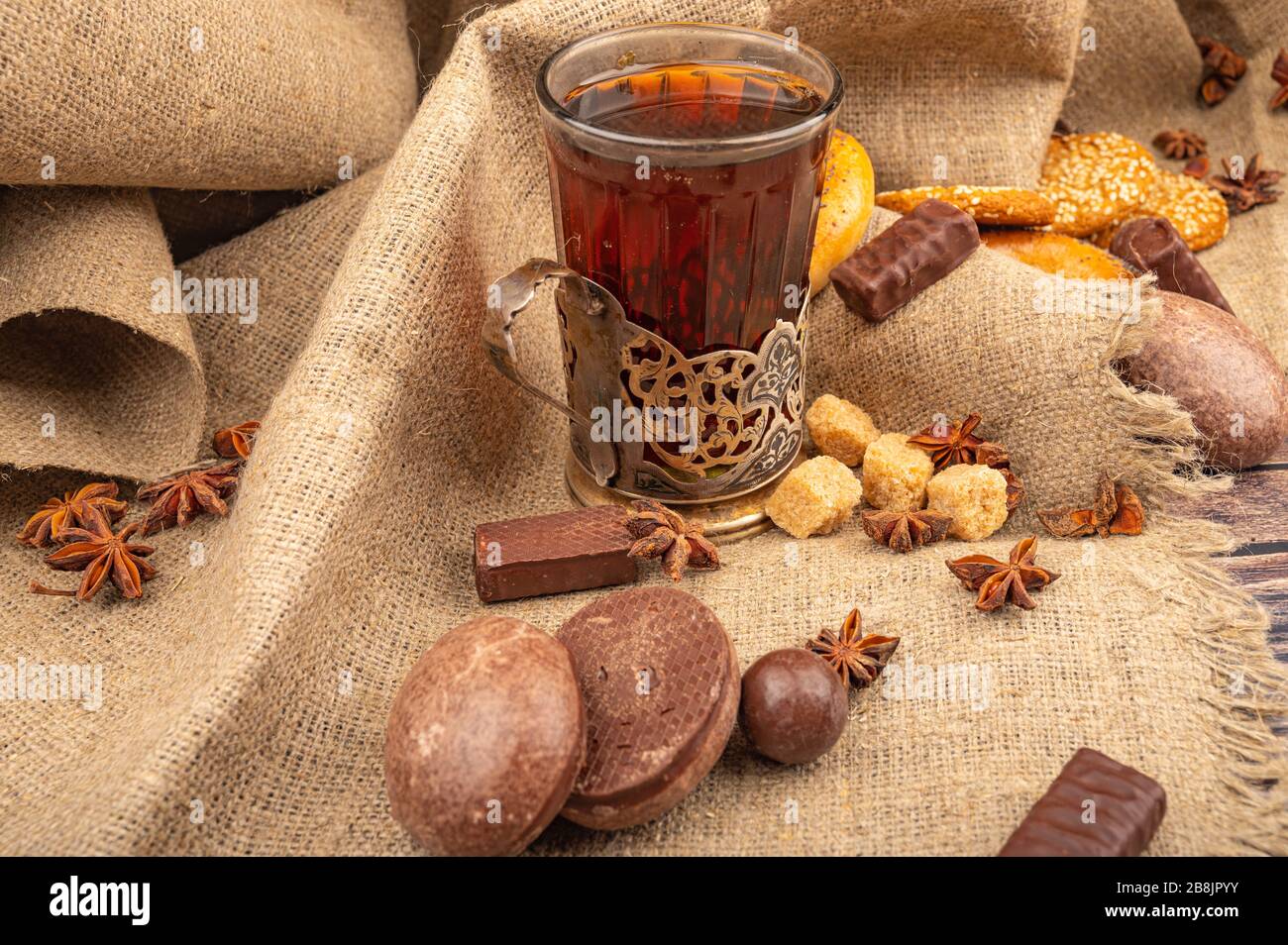 Un verre à facettes de thé dans un porte-gobelet millésime, des biscuits, des gâteaux au chocolat et du chocolat sur fond de tissu texturé. Gros plan Banque D'Images