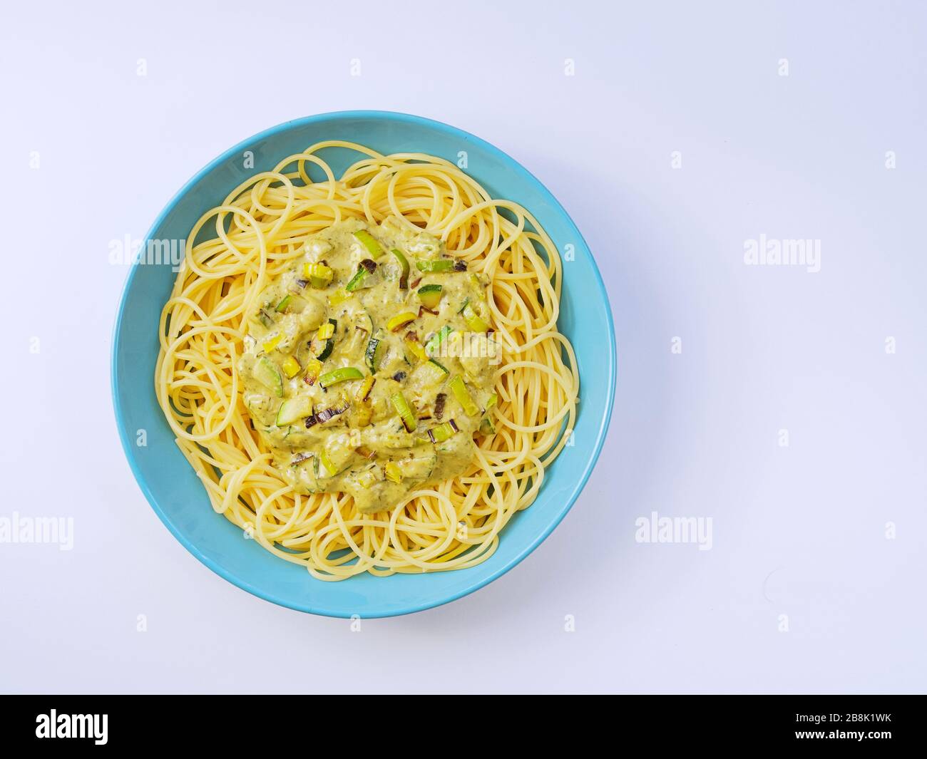 Spaghetti avec une sauce crème avec courgettes et poireaux dans une assiette bleu clair sur fond blanc d'en haut. Banque D'Images