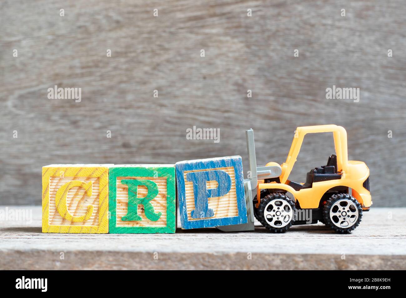 Le chariot élévateur à fourche jouet tient le bloc de lettres P pour compléter le mot CRP (abréviation de C-réactif Protein Test) sur fond de bois Banque D'Images