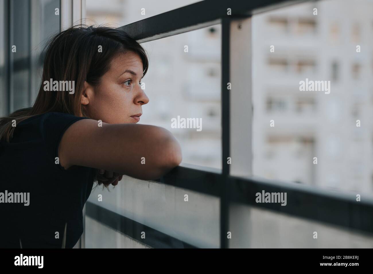 Jeune femme triste regardant à l'extérieur par balcon d'un immeuble d'appartements Banque D'Images