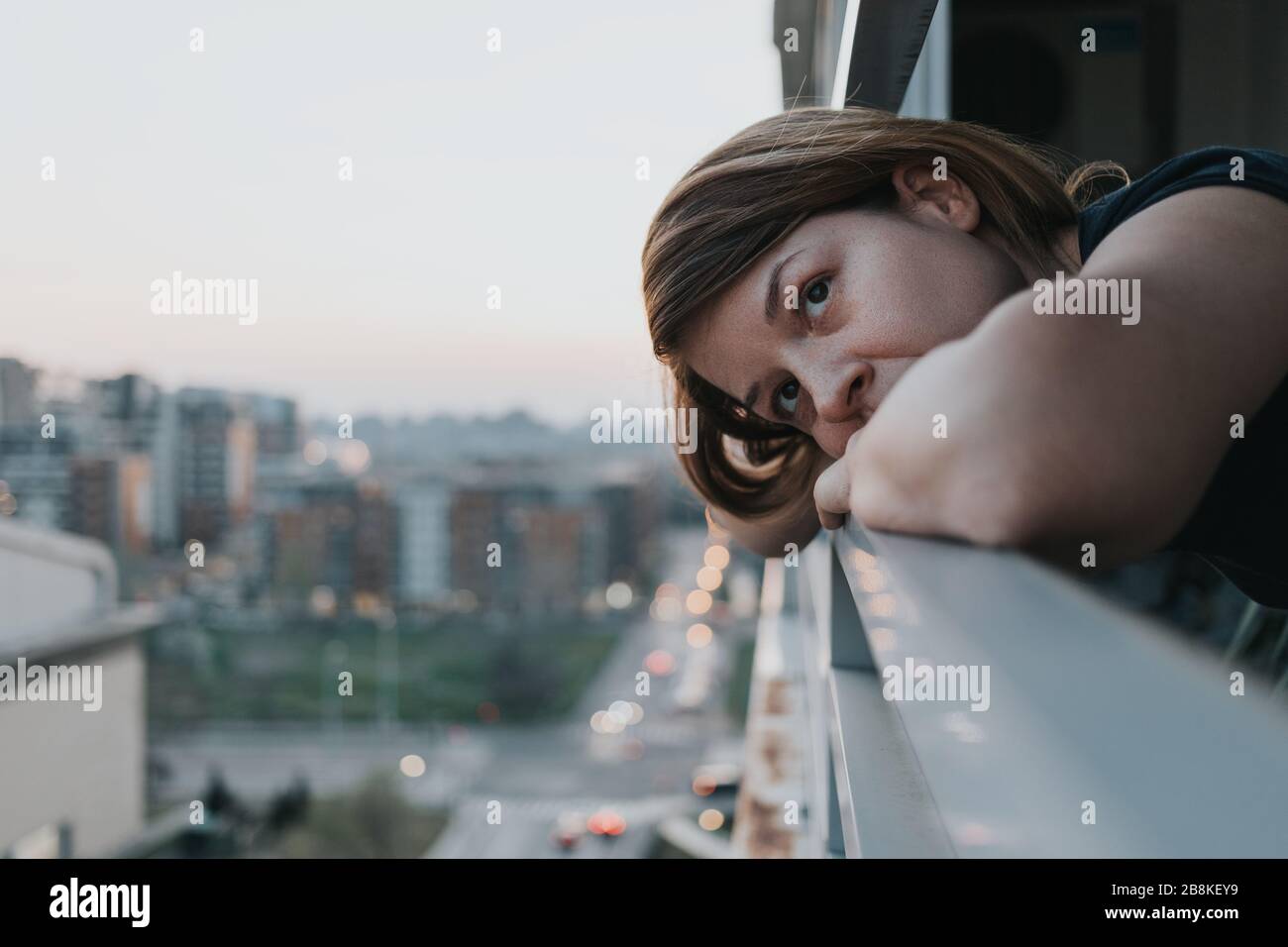 Jeune femme triste regardant à l'extérieur par balcon d'un immeuble d'appartements Banque D'Images