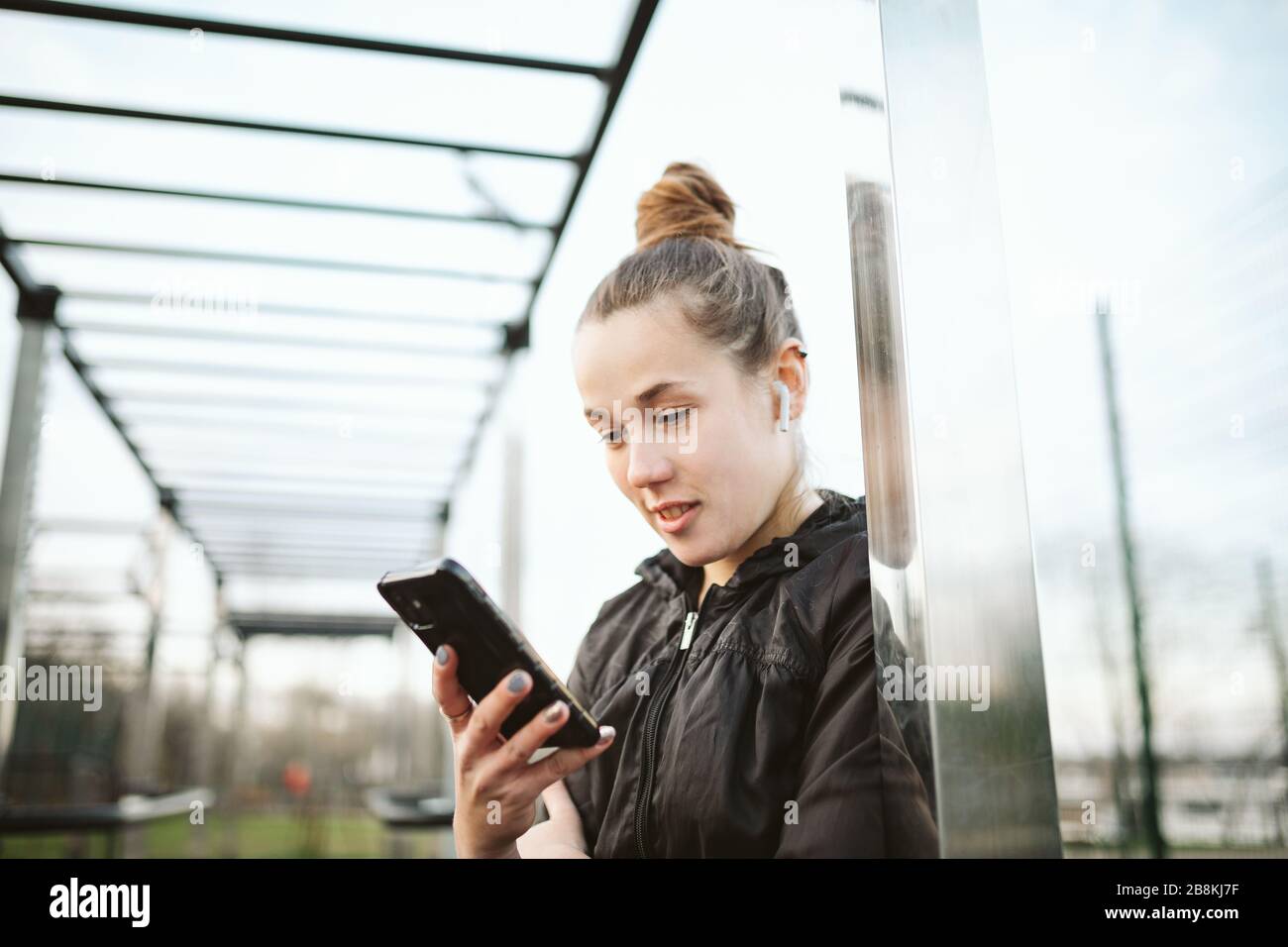 Femme athlète dans les tatouages, en ville, se reposant après l'entraînement physique, l'entraînement. Casque smartphone. Réseaux sociaux d'applications en ligne. Écoute Banque D'Images