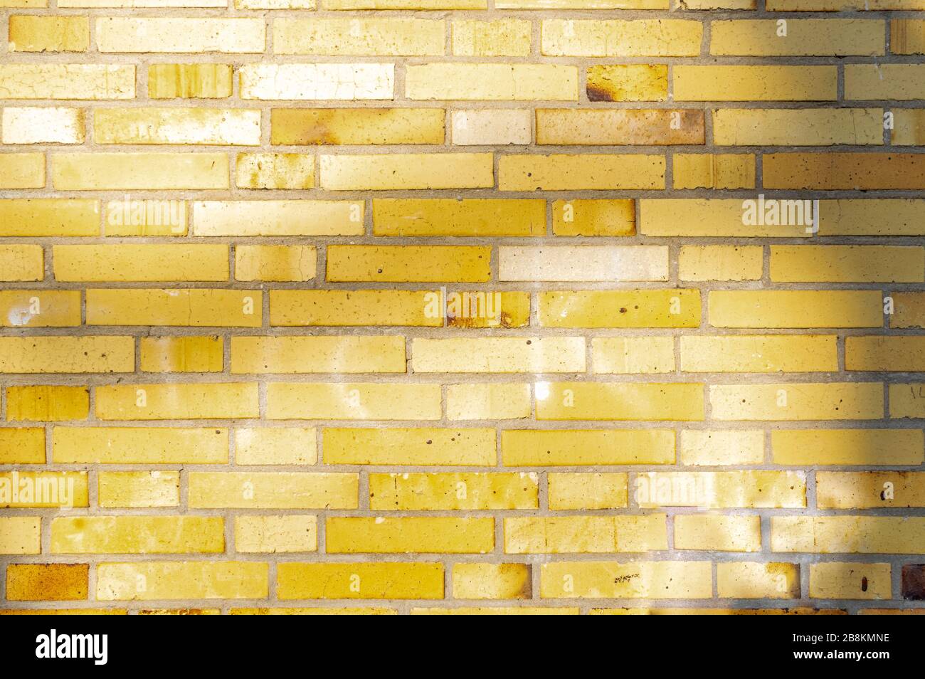 Section d'un vieux mur de bâtiment partiellement abîmé et pollué de briques de clinker jaune à brunâtre avec des ombres douces d'arbres Banque D'Images