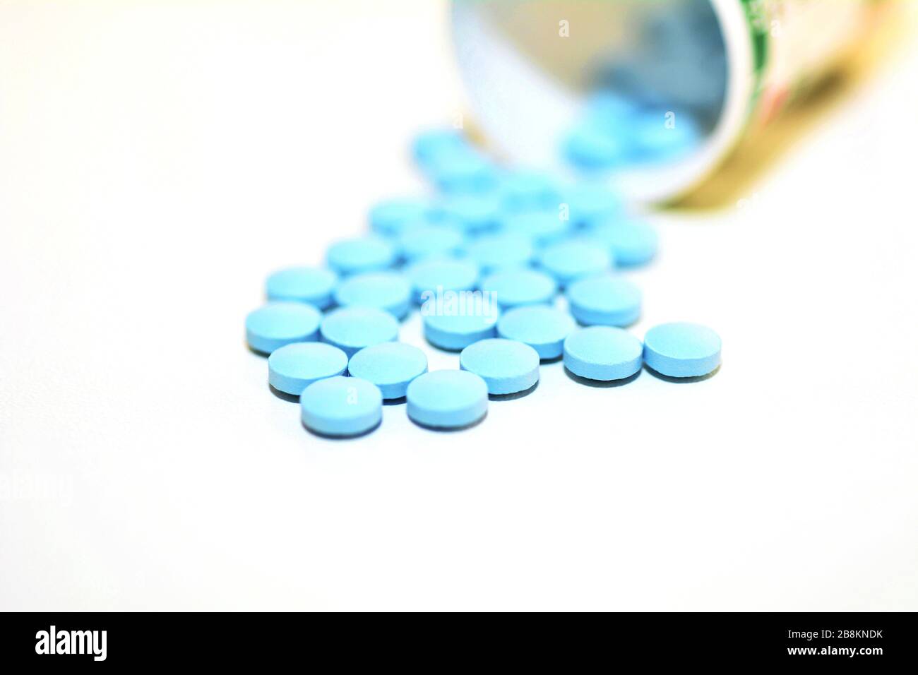 Gros plan d'une pilule de médicament bleu qui déborde d'une bouteille sur le fond blanc. Banque D'Images