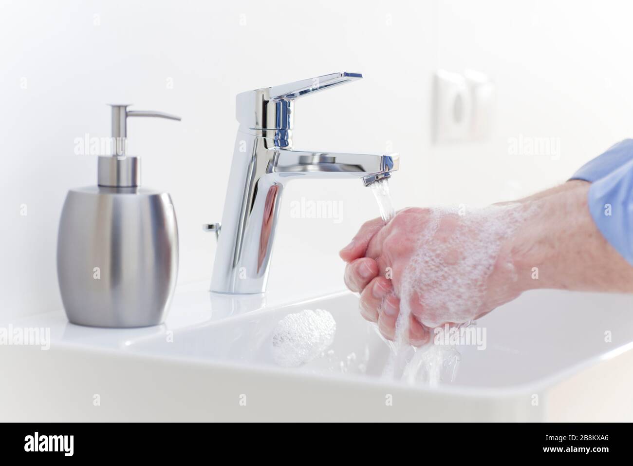 L'homme se lavant les mains avec du savon liquide dans une salle de bains blanche pour se protéger contre l'infection - foyer sélectif sur le robinet Banque D'Images
