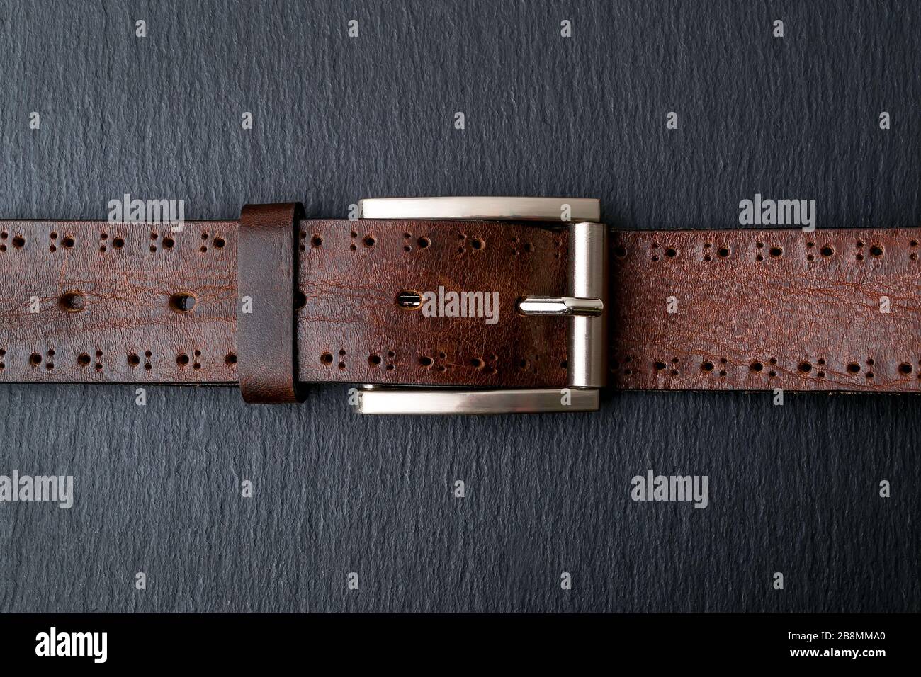Ceinture en cuir marron authentique avec boucle en métal classique sur fond noir. Accessoires en cuir élégants pour Homme. Image de touche basse. Vue de dessus. Banque D'Images