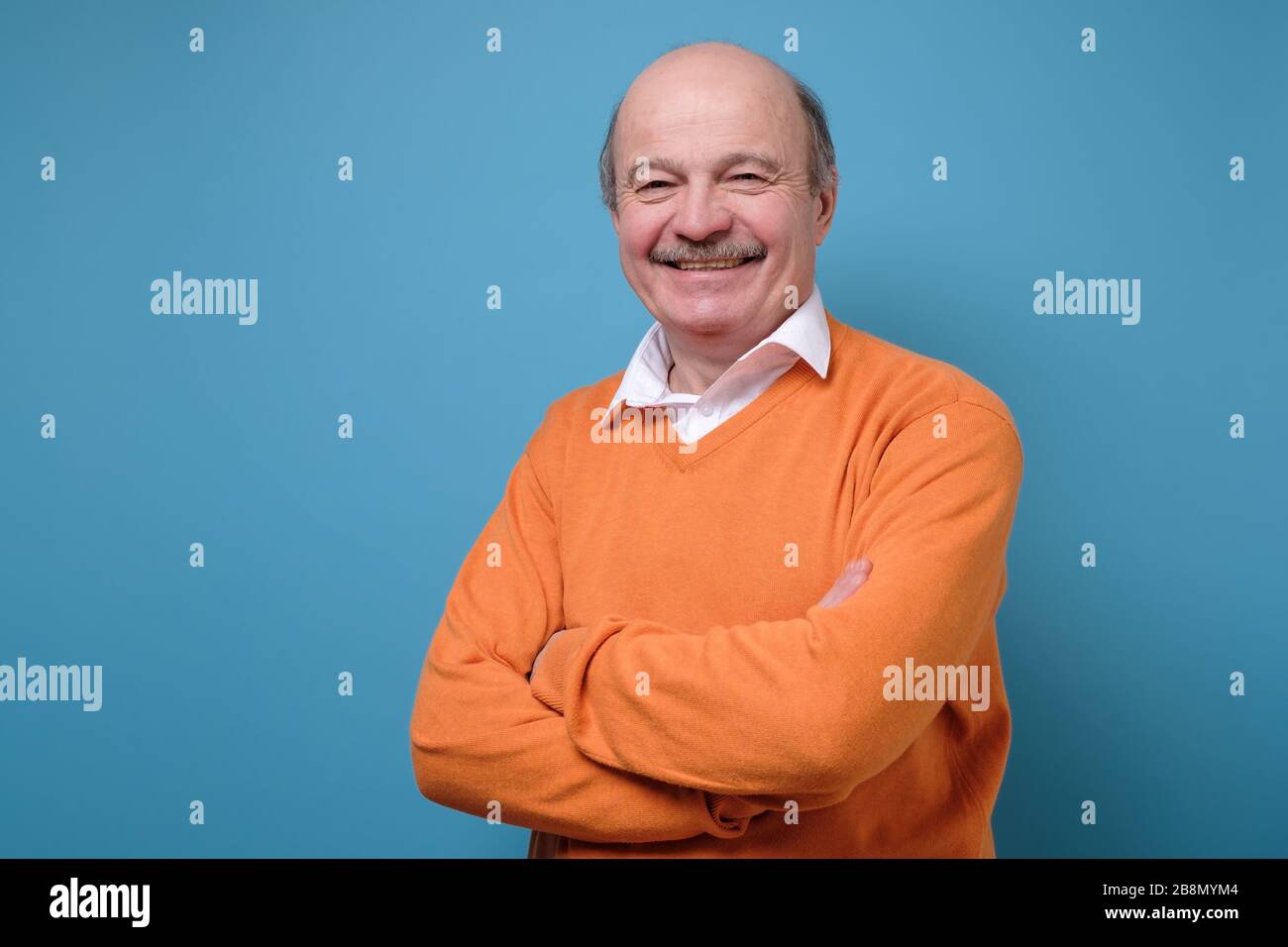 Souriant mûr décontracté homme en chandail orange isolé sur bleu arrière-plan Banque D'Images
