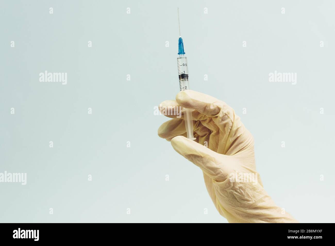 La main du médecin dans un gant en caoutchouc blanc contient une seringue médicale sur un fond bleu. Le concept de médecine et de soins médicaux pour le patient. Banque D'Images