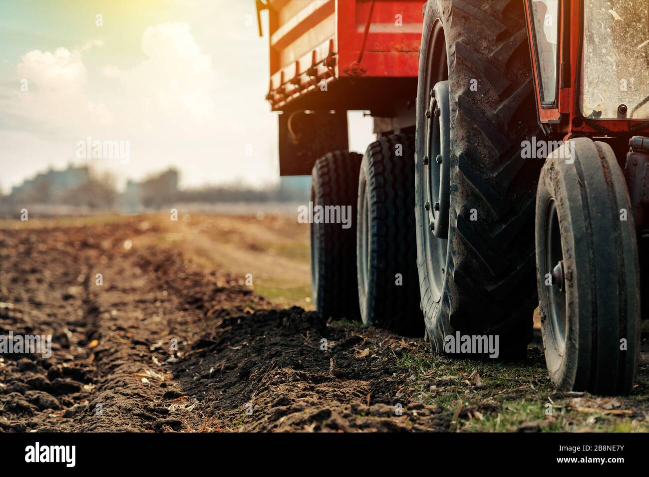 Vieux tracteur agricole rouge avec remorque sur la saleté route de campagne au printemps après-midi Banque D'Images