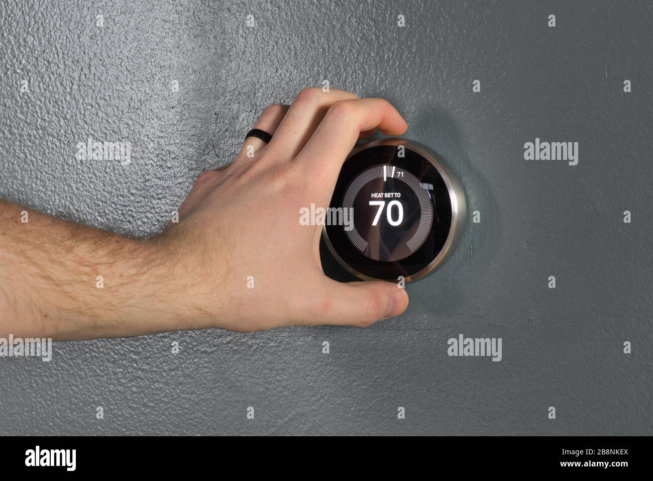 Le thermostat domestique intelligent Nest ajusté par les utilisateurs à la main. Appuyez sur le bouton central et sur le cadran pour économiser de l'argent sur le chauffage et le refroidissement des technologies vertes Banque D'Images