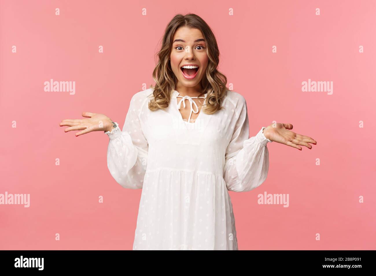 Surprise et heureuse jeune fille blonde réaliser qu'elle a gagné, recevoir vraiment de bonnes nouvelles, se répandre les mains sur le côté souriant et regarder étonné de l'appareil photo, debout rose Banque D'Images