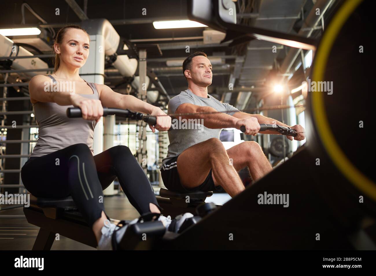 Vue en bas angle sur un couple sportif utilisant des appareils d'exercice pendant l'entraînement de force dans une salle de sport moderne, espace de copie Banque D'Images