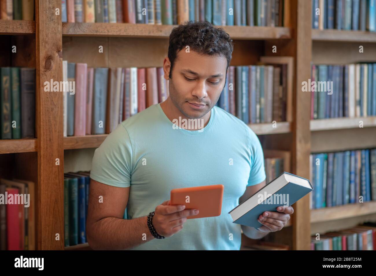 Homme aux cheveux sombres avec une tablette dans les mains regardant le livre Banque D'Images