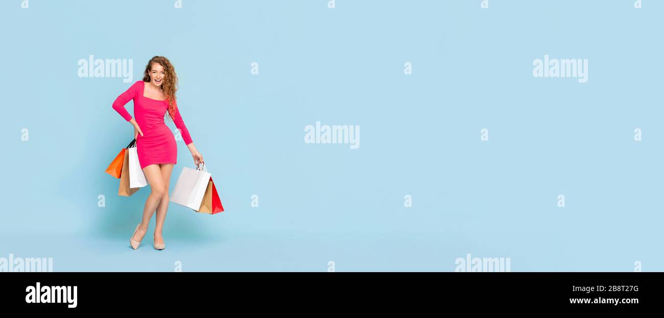 Femme caucasienne souriante avec des sacs de shopping colorés debout sur fond de bannière isolée bleu clair avec espace de copie Banque D'Images