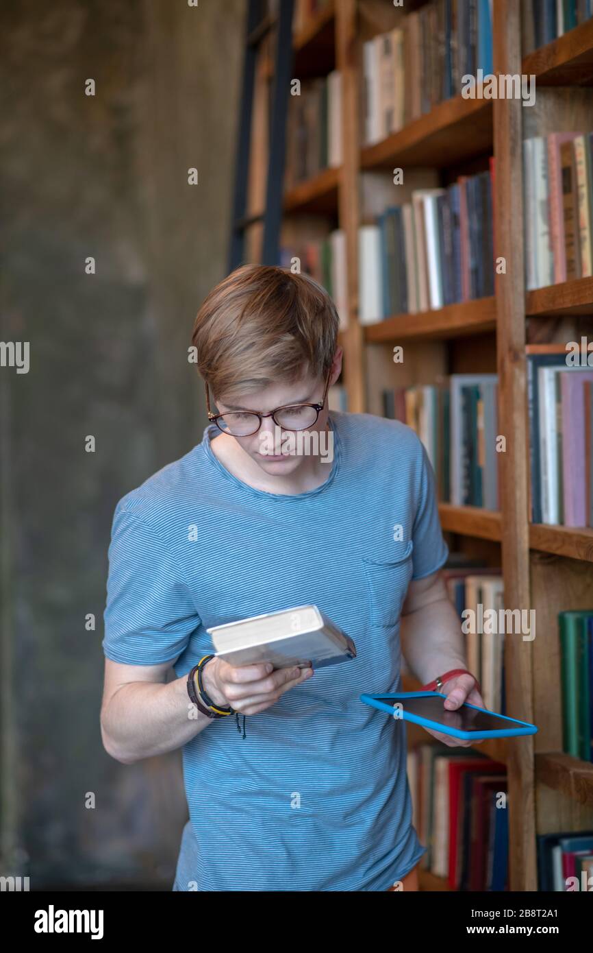 Jeune homme dans des lunettes regardant le livre dans sa main Banque D'Images